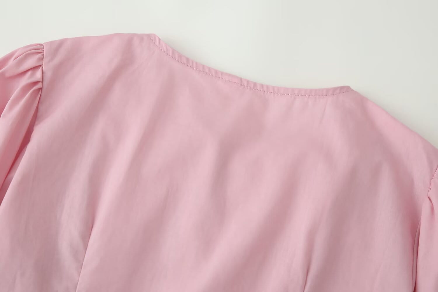 A soft pink lightweight cotton dress featuring a gentle ruffled neckline and puffed short sleeves with a slim-fit design and round neckline.