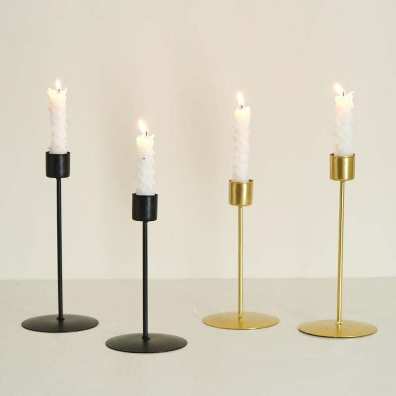 Set of four minimalist metal candle holders in black and gold finishes each holding a white textured taper candle for golden European style home decor.