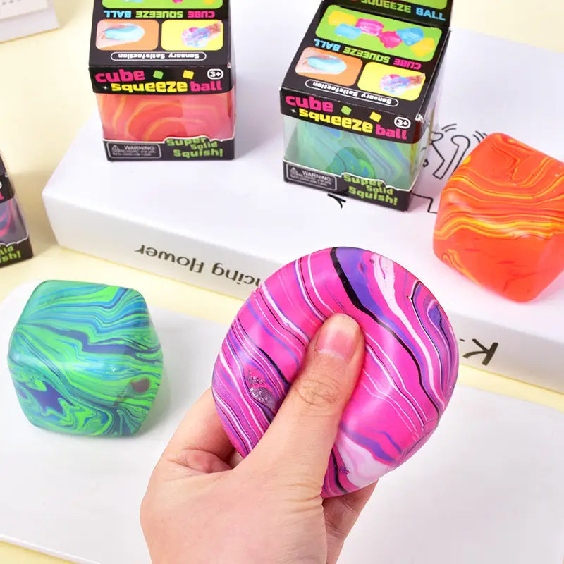 A hand holds a vibrant pink and purple marble swirl cube squeeze toy made of soft squishy material designed for slow rising sensory fidget use.