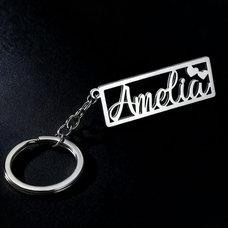 Silver metallic custom name stainless steel keychain with the name amelia cut out in elegant cursive script and two small heart accents on a rectangular plaque.
