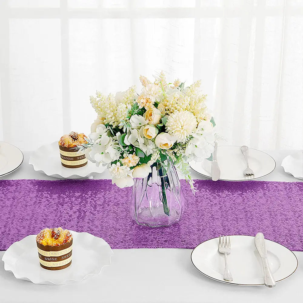A clear faceted glass vase with a bouquet of white and cream flowers displayed on a sequin table runner 12x72 inch party decor.