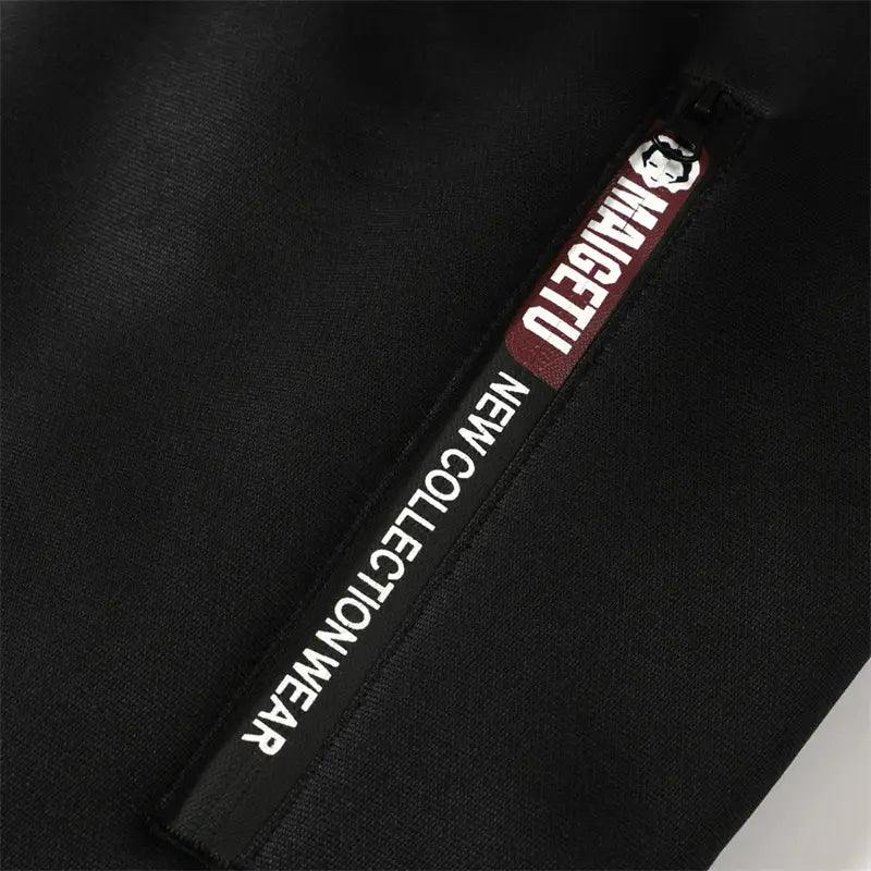 黒い生地のタグ。白文字で「maigetu new collection wear」と記載され、メンズのシェルパ裏地付きウィンタージップフーディに小さなロゴが付いています。