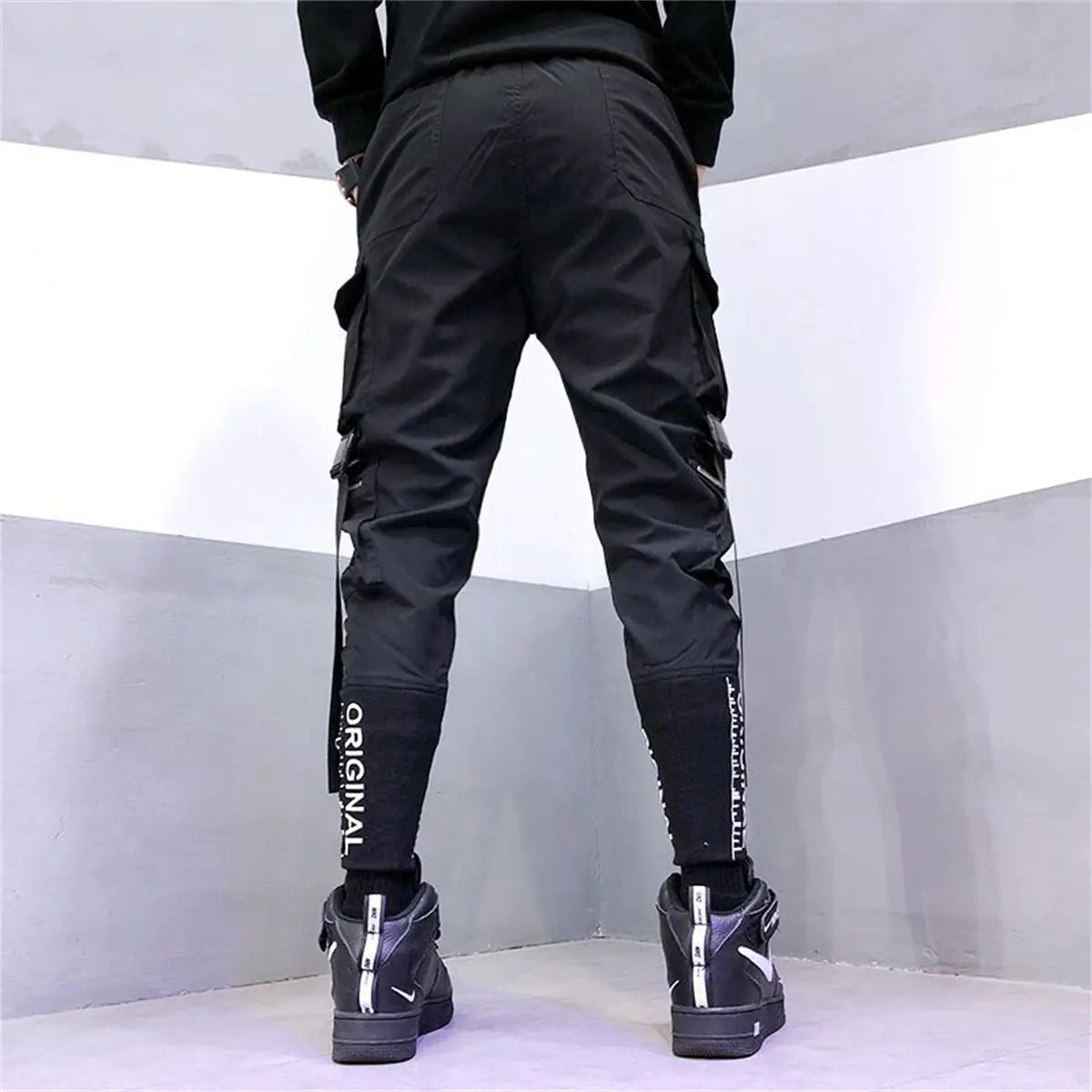 Pantalons cargo tactiques pour hommes noirs, dotés de plusieurs poches latérales et d’un marquage vertical blanc le long de la jambe extérieure, conçus pour le techwear et le streetwear.