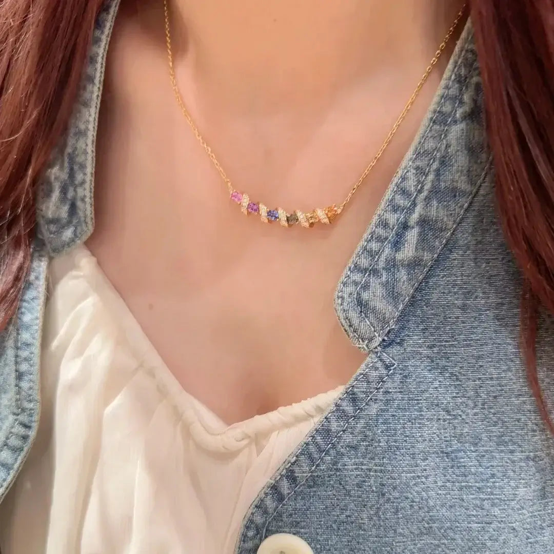 Un collier en argent présentant une chaînette délicate en or, avec une rangée de pierres précieuses facettées colorées en rose, violet, vert et jaune, dans un design de pendentif géométrique.