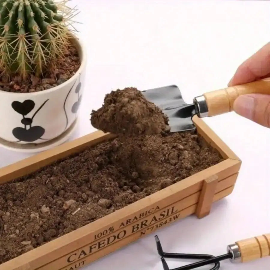 Jardinera rectangular de madera con texto grabado 100 por ciento arabica cafedo brasil junto con un pequeño cactus en una maceta blanca, presentada con un set de herramientas de jardinería en miniatura con mango de madera de 3 piezas