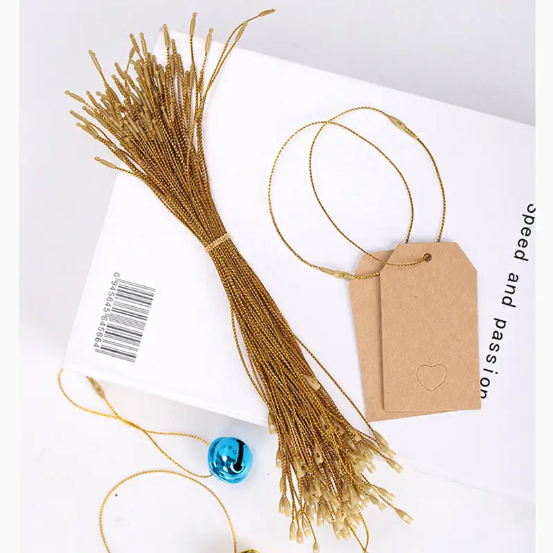 goldfarbene metallische Aufhängeseile mit dezentem Schimmer, gebündelt zusammen, und begleitet von Kraftpapier-Anhängern für Weihnachtsbaum-Ornamente.
