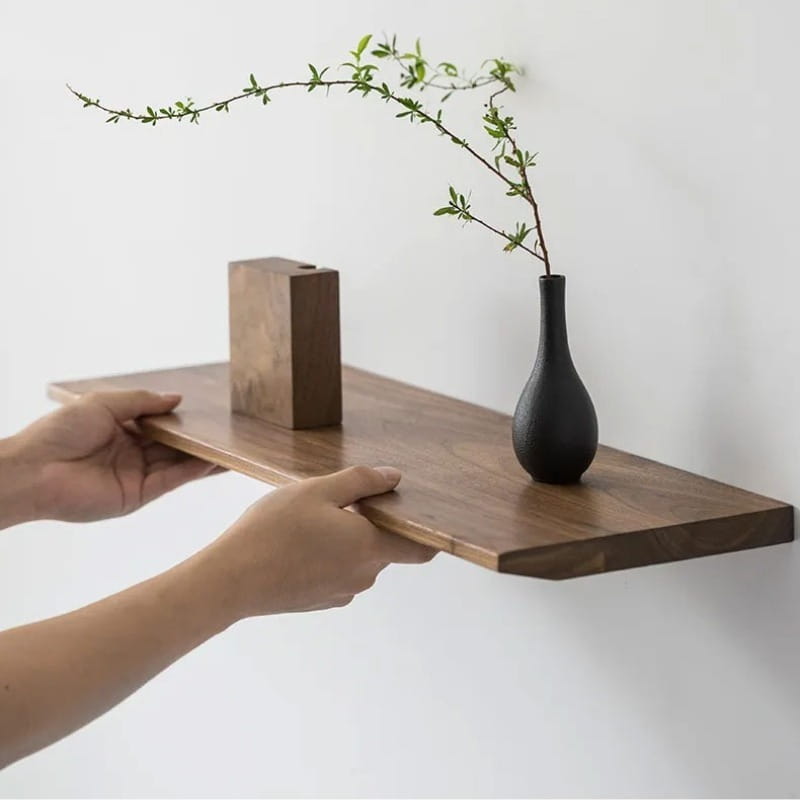 dark matte black ceramic vase with slender neck and rounded body holding a green branch displayed on wall farmhouse wooden shelves live edge wooden shelves.