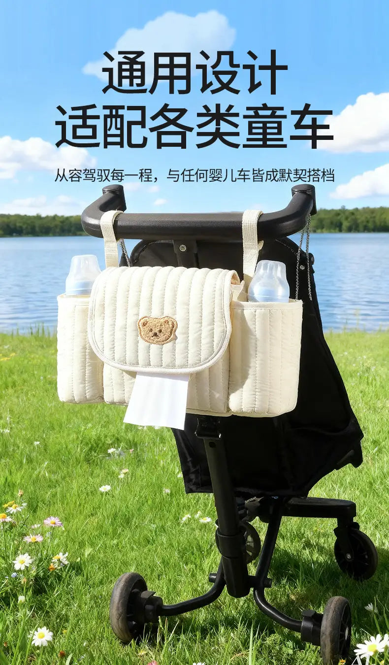 Cremefarbener wattierter Kinderwagen-Organizer-Beutel mit Teddy-Applikation und mehreren Taschen für eine praktische Aufbewahrung.