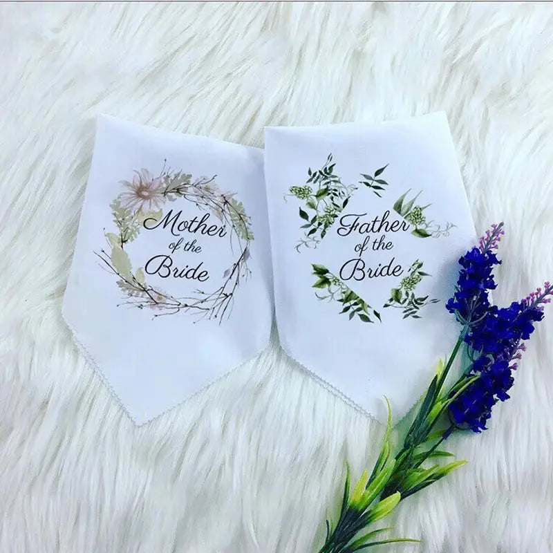 weiße dreieckige Halstücher in einem Set für ein Hochzeits-Taschentuch der Eltern, das eine Aufschrift mit der Mutter der Braut und dem Vater der Braut enthält, gedruckt in schwarzer geschwungener Schrift innerhalb von floralen Kränzen mit zarten rötlich-rosa Farbtönen sowie Designs mit grünen Blattmotiven.