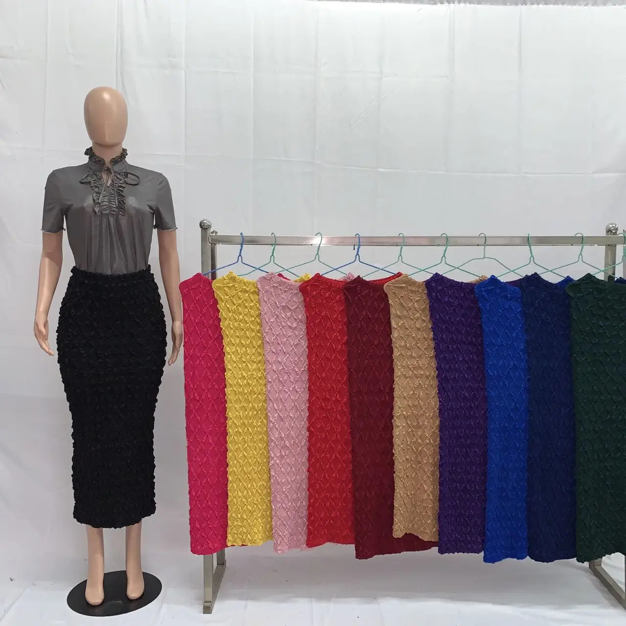 Black high waist knit midi skirt with textured slim fit displayed on a mannequin beside a rack of colorful knit skirts.