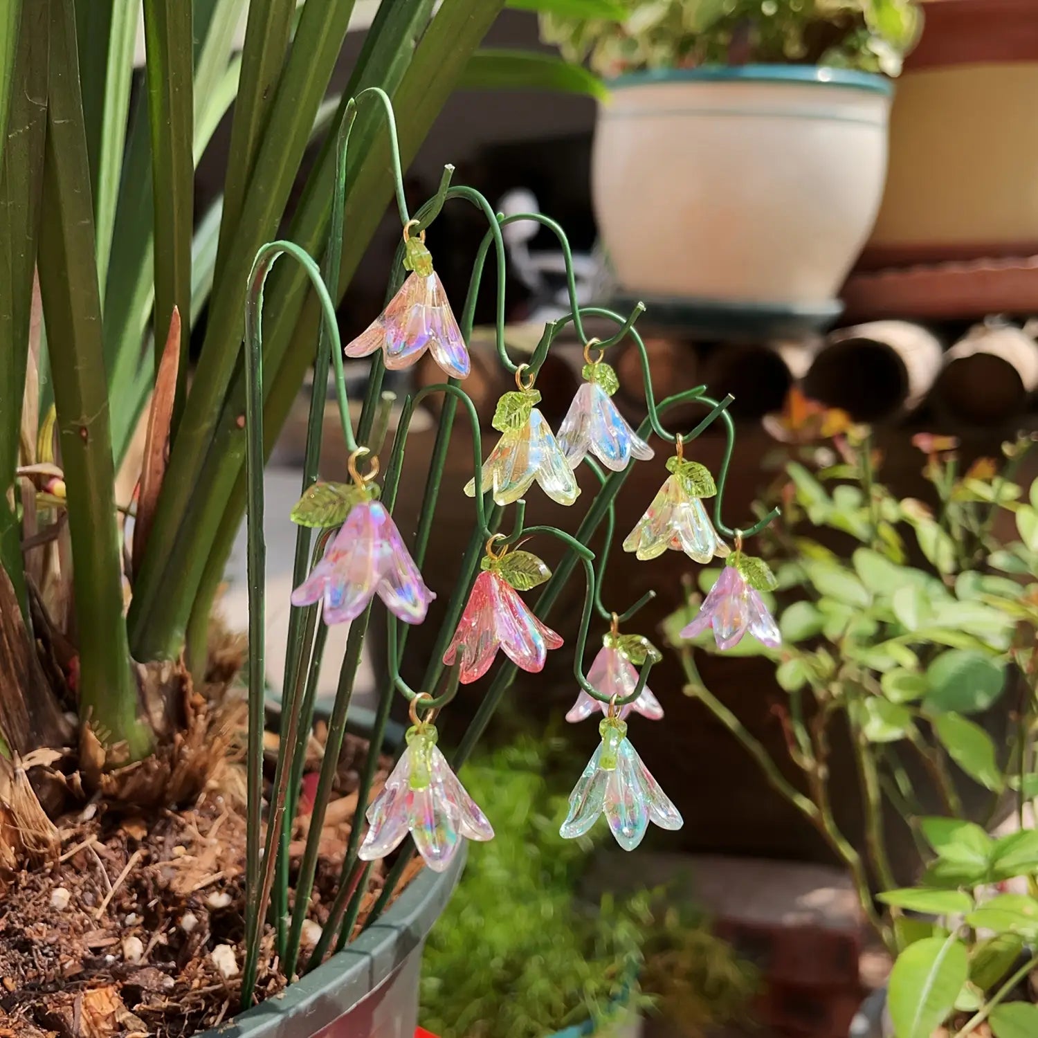 Iridrescent glass lily garden stakes plant decor featuring bell-shaped ornaments with tiny green leaves dangling from a curved wire frame.