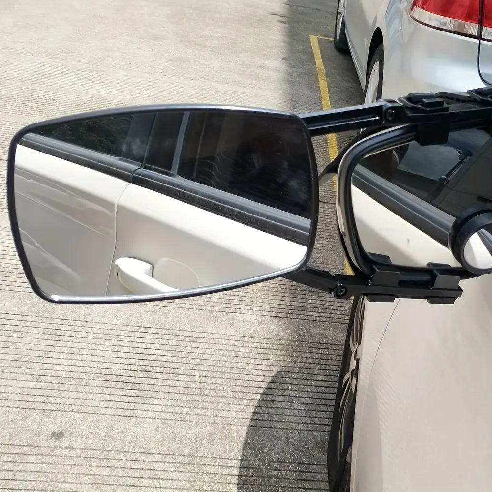 Clip negro de posventa para la extensión del retrovisor de enganche, con superficie reflectante rectangular y brazo ajustable instalado en un automóvil blanco para el uso en autocaravanas y camiones.