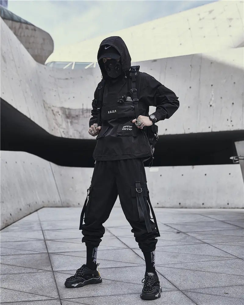 Veste tactique techwear noire fabriquée dans un matériau imperméable, avec capuche, poches avant et sangles réglables pour un usage extérieur polyvalent.