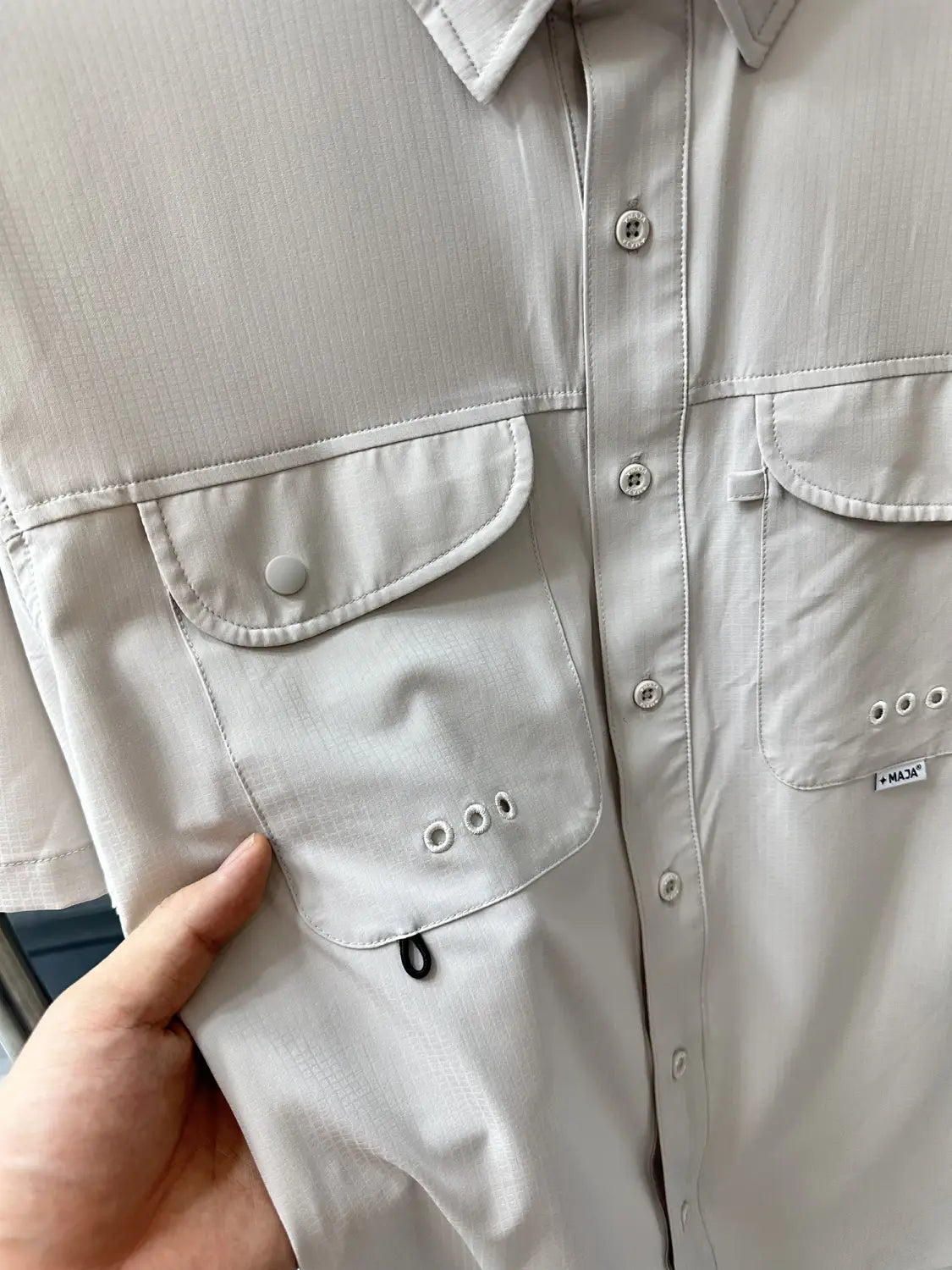 Ein hellgraues Herren-Stretch-Outdoorhemd mit schnelltrocknender Funktion mit Knopfverschluss vorne, zwei Taschen mit Druckknopf-Schließe und subtilen Ziernähte-Details.