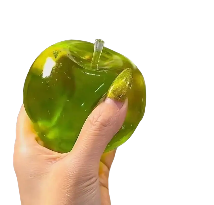 une balle anti-stress souple verte en forme de pomme translucide, avec une tige transparente tenue par une main, avec un vernis à ongles doré scintillant.