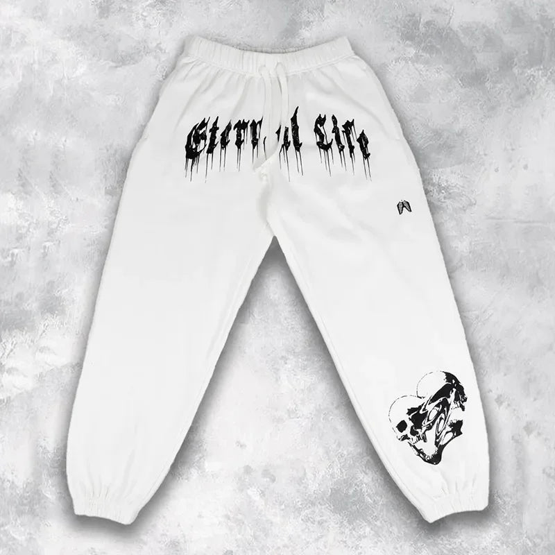 Pantalons d’entraînement graphiques pour hommes, sweatpants blancs, avec un texte style graffiti noir « ghettos of life » sur la ceinture et un graphisme de crâne sur la partie inférieure de la jambe.