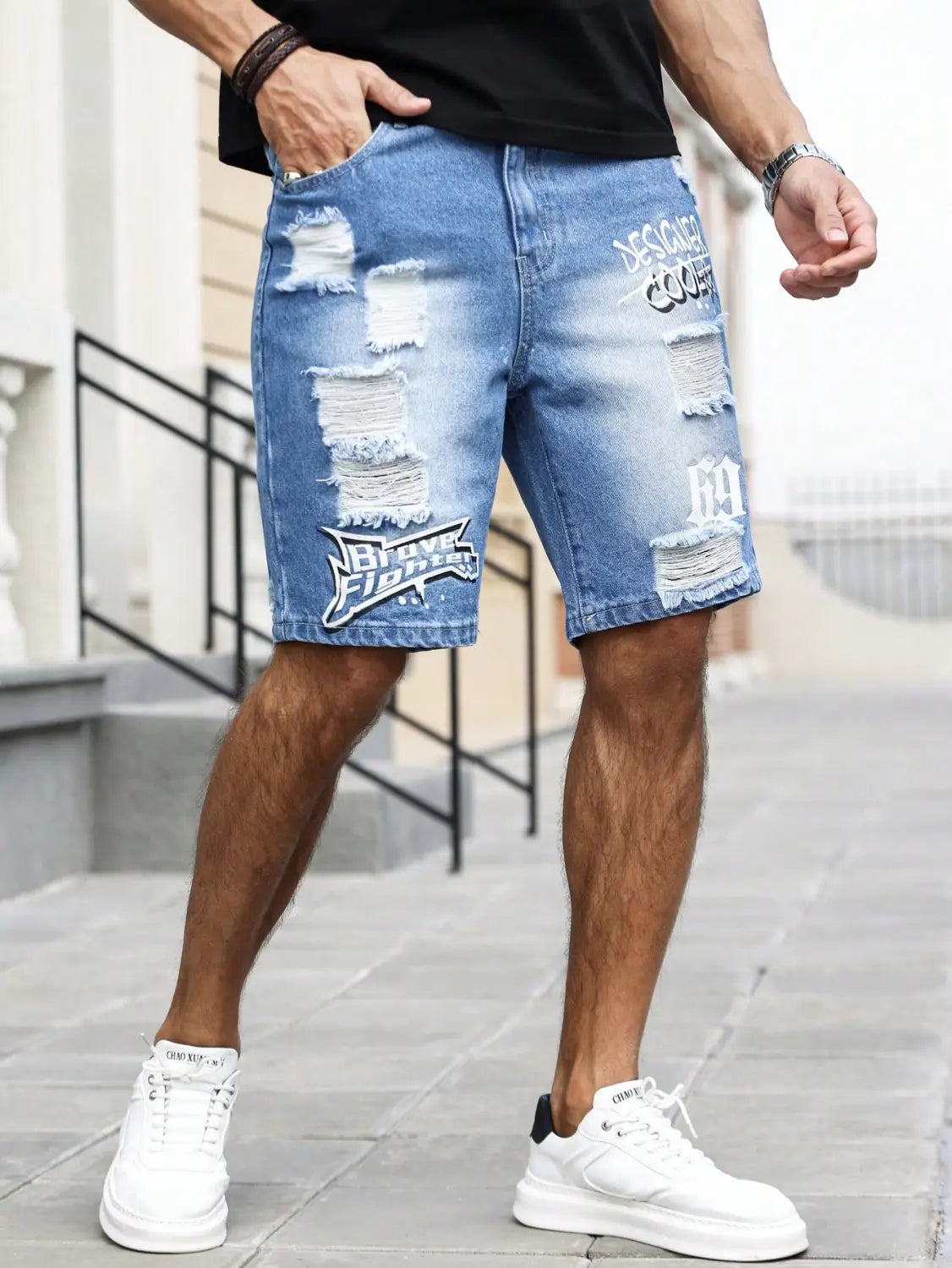 Shorts en jean bleu déchirés pour hommes, avec un délavage vieilli, présentant plusieurs patchs abîmés aux bords effilochés et des graphismes brodés, y compris « nba » et « 1984 », pour une tenue d’été.