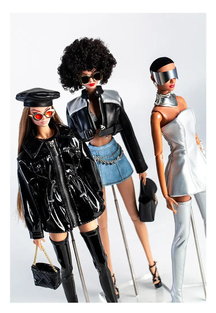 Drei modische Barbie-Puppen in 1/6-Skala futuristischer Puppenbekleidung und Accessoires, mit einer glänzenden schwarzen Lacklederjacke und kniehohen Stiefeln mit schwarzer, gesteppter Handtasche, einem silbermetallischen Oberteil mit hochtaillierten Jeansshorts und passendem Gürtel, mit jeweils unverwechselbaren stilvollen Ensembles.