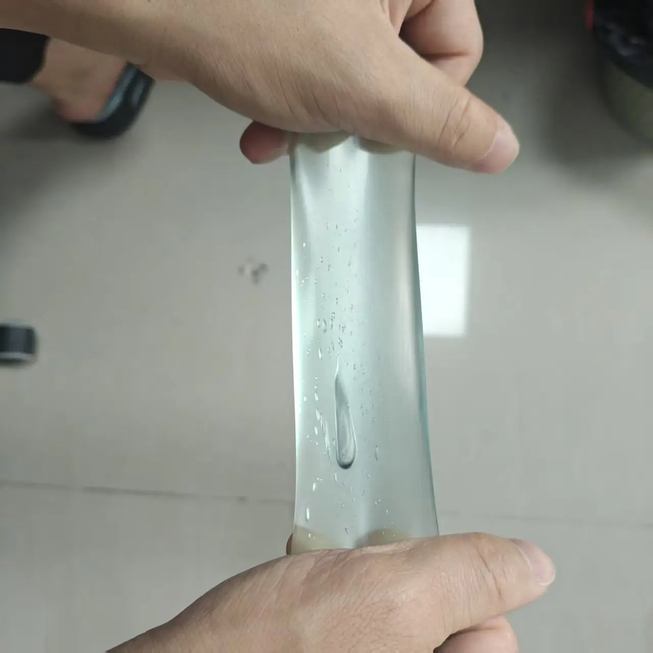 une balle anti-stress souple transparente verte, jouet sensoriel, contenant une substance légèrement visqueuse de type gel, étirée entre deux mains.
