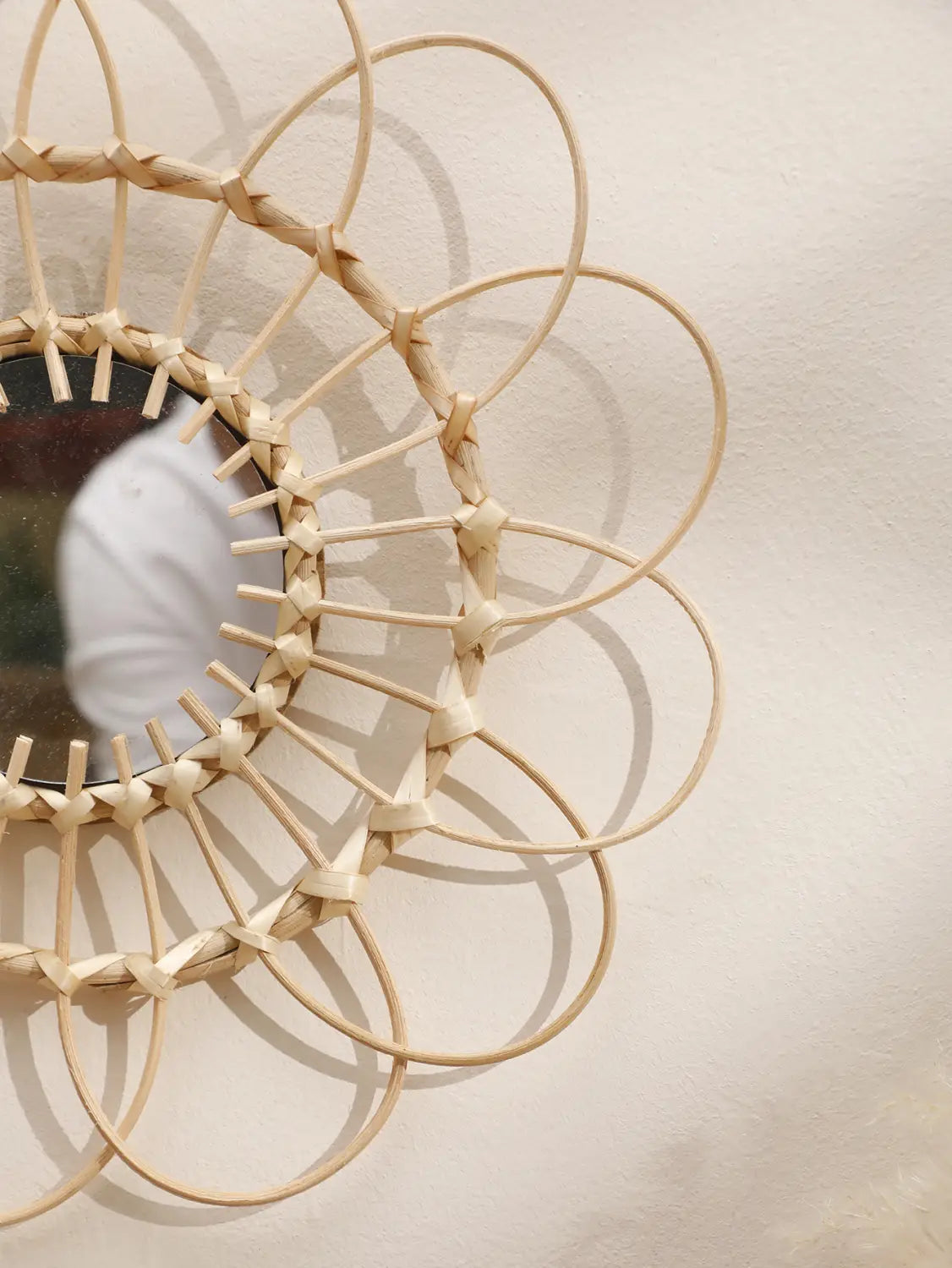Ein zarthellbeiger, gewebter Rattan-Sonnenstrahl-Wandspiegel mit rundem Rahmen, mit kunstvollen überlappenden Schlaufen und diamantförmigen Knoten, ideal für die ästhetische Gestaltung des Raums.