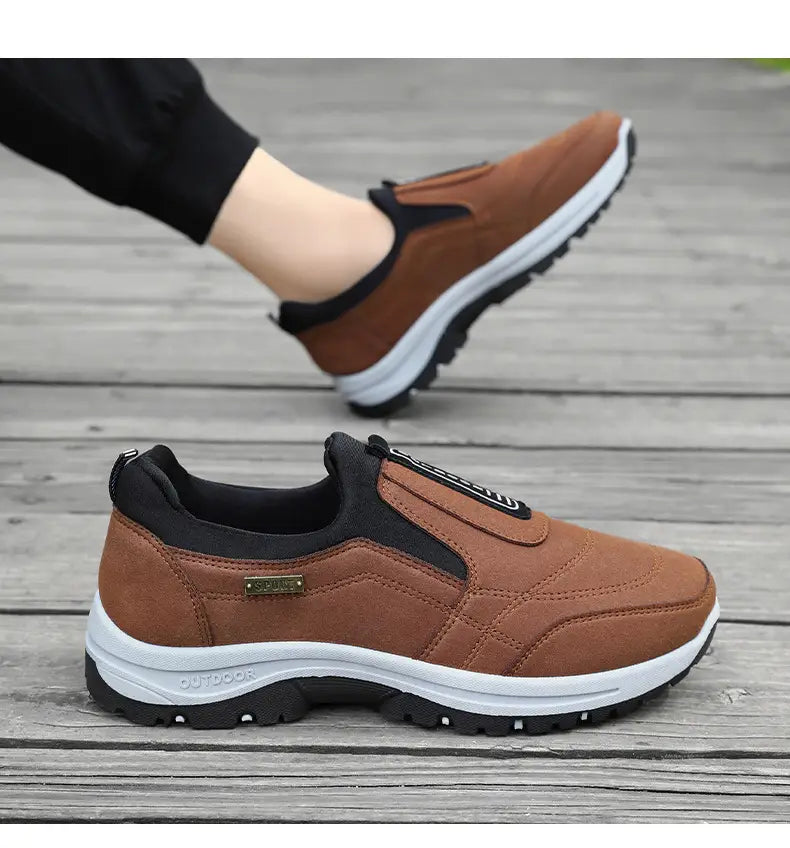 men orthopedic slip-on walking shoes showing the back side of brown suede and black mesh sneakers with a white midsole black outsole and an outdoor label on the heel.