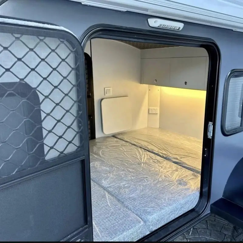 Gray custom teardrop travel trailer fully equipped camper showing the back side with a mesh door panel and interior bed covered in protective plastic.
