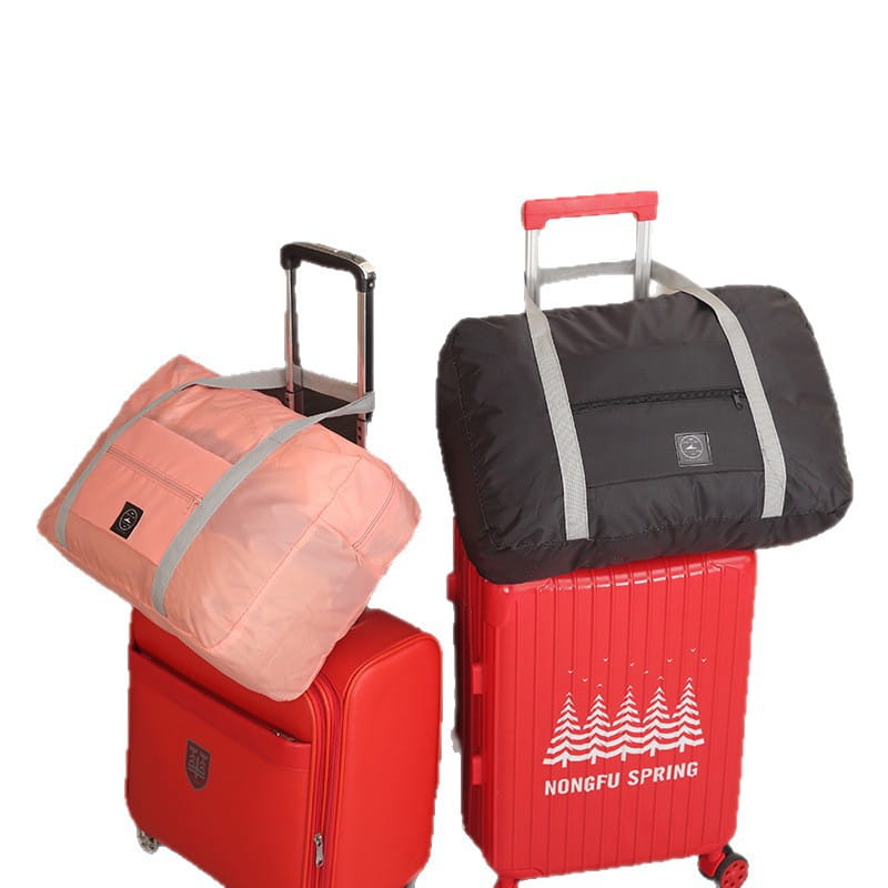 Juego de bolsa de lona de viaje plegable con bolsas plegables rosas y negras, con correas grises, apoyadas sobre maletas rojas.