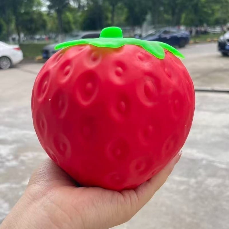 A vibrant red textured strawberry-shaped jumbo slow rising sensory fidget toy with a bright green leafy top designed as a stress ball.
