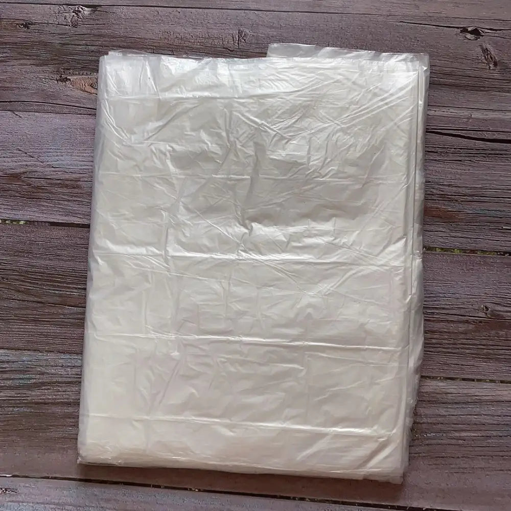 Eine durchscheinende, zerknitterte off-weiße Kunststoff-Möbel-Staubabdeckung als Schutzhülle, flach auf einer Holzoberfläche liegend.