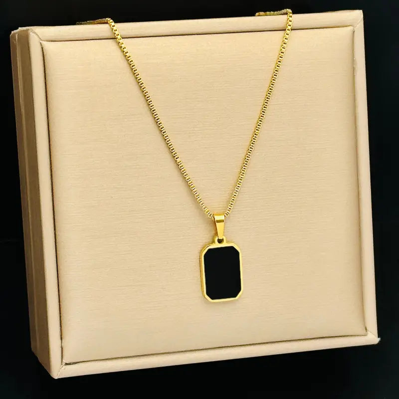Collier médaillon rectangle en or pour femmes, avec une chaîne fine à maillons boîte ton or et un pendentif rectangulaire en émail noir.