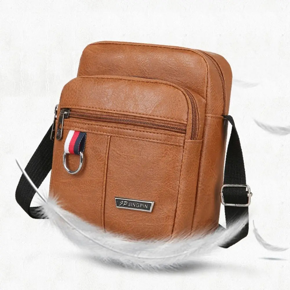 Sac messager bandoulière en cuir brun avec sangle noire et accent rayé rouge, blanc et bleu, conçu comme un sac messager bandoulière pour hommes pour un usage décontracté