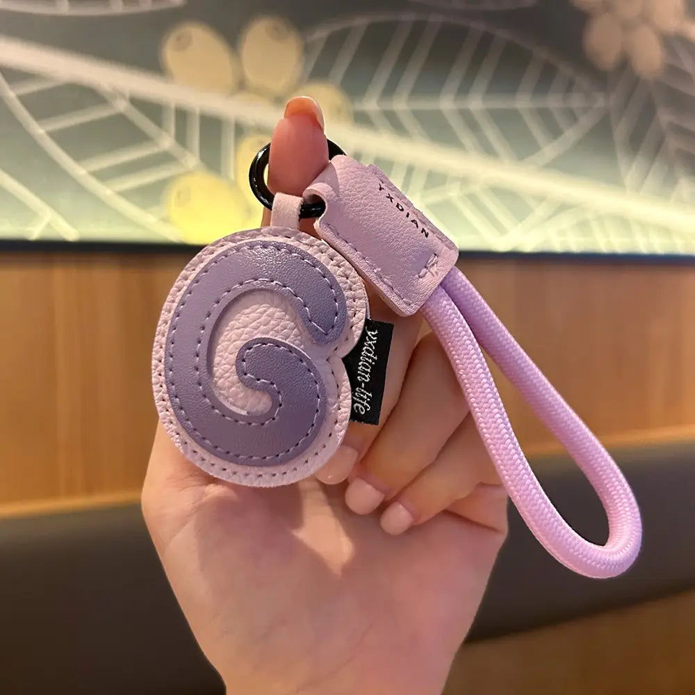 A lavender leather initial keychain letter wristband charm featuring a circular stitched letter g design with a matching fabric loop and tag.
