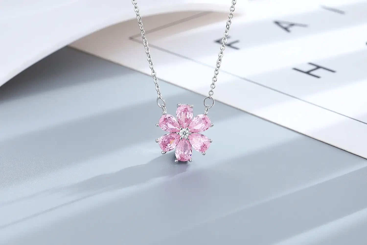 Eine zarte Silberkette mit Kettenanhänger in Form einer pinkfarbenen Kirschblüte mit facettierten Steinen und einem zentralen, klaren Stein aus dem Schmuckset „Silber Pink Kirschblüte“.