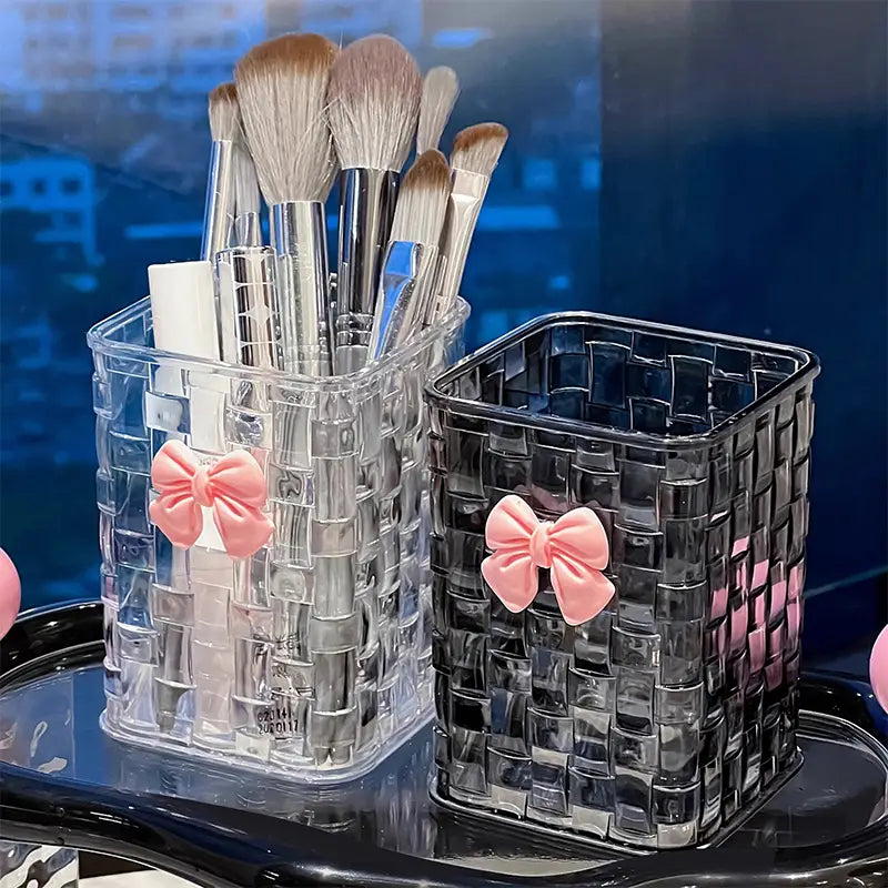 Bow pen holder desktop storage organizer featuring clear and black woven-patterned makeup brush holders each adorned with a pink satin bow.