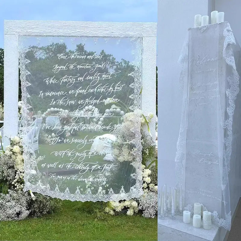 Weiße, mit Spitze eingefasste transparente Hochzeitskulisse mit eleganter kursiver Schrift und floralen Arrangements für ein individuelles Willkommensschild aus Spitze als Banner.
