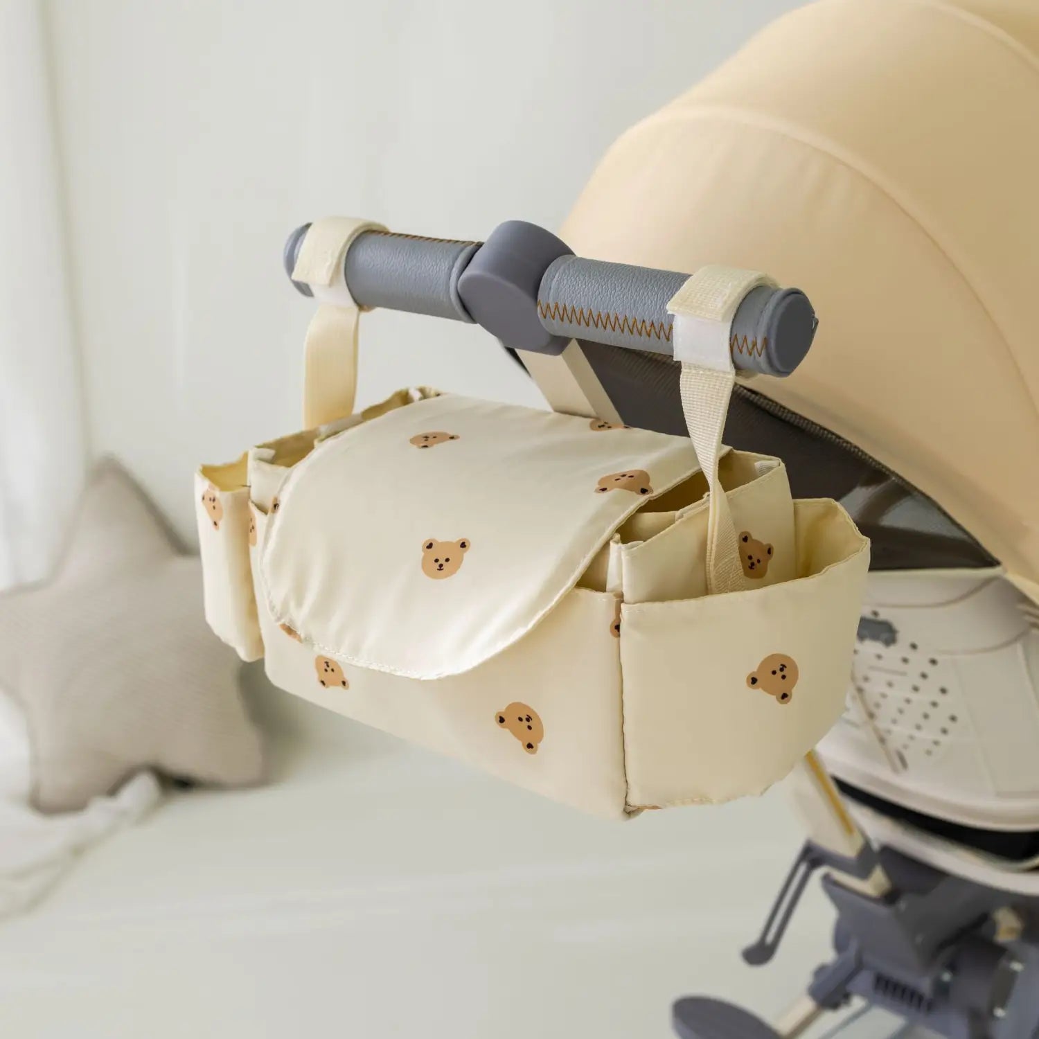 小さな茶色のクマのプリントをあしらったクリーム色のベビーカー用オーガナイザーバッグ。複数のコンパートメントで、便利に収納できます。