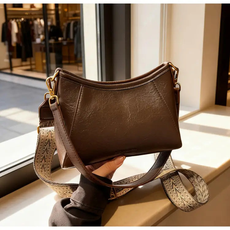 柄のあるストラップとゴールドトーンの金具を備えた、女性用ブラウンレザーのクロスボディショルダーバッグ。
