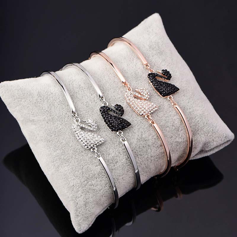Trois bracelets jonc élégants avec breloque de cygne en cristal, ornés de designs étincelants sertis de cristaux en argent, or rose et noir, avec des accents de strass.