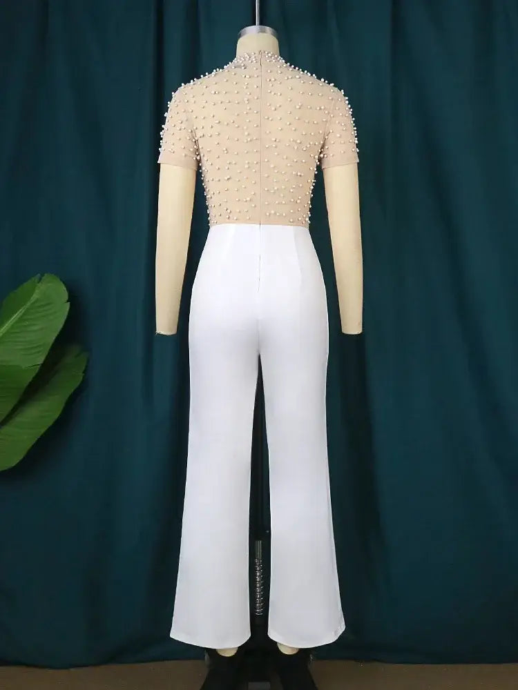 Beige beaded short-sleeve top paired with white high-waisted flared pants in an elegant party outfit jumpsuit.