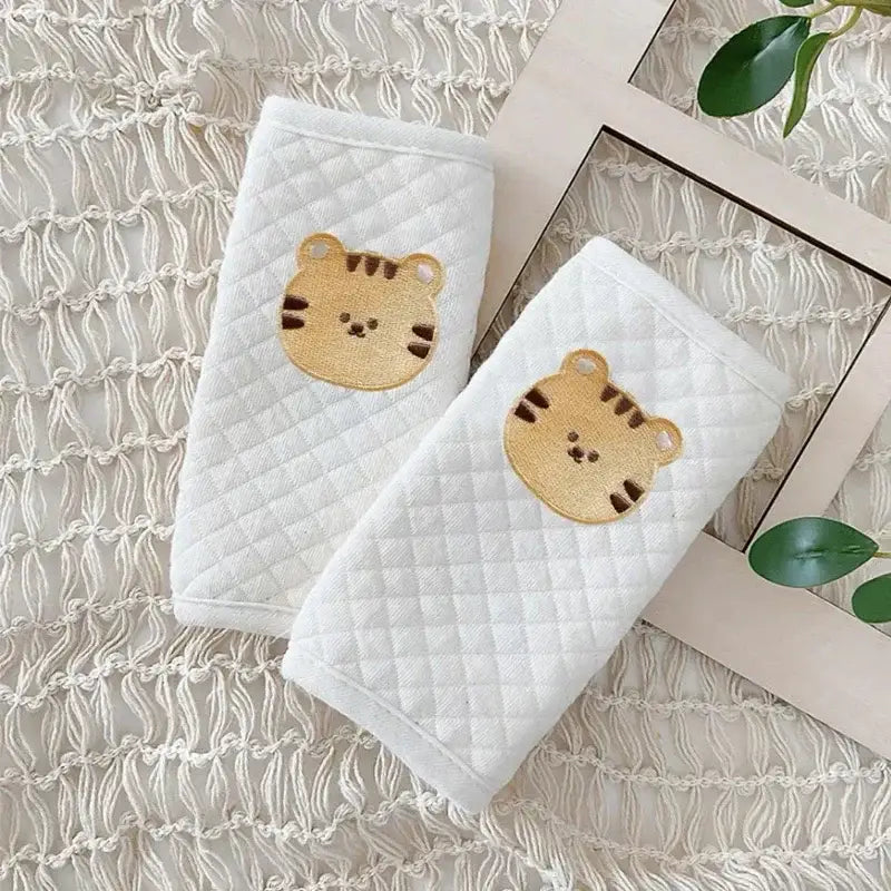リストバンドに刺繍したタン（こげ茶寄り）のトラの顔が特徴の、白のキルティング加工ベビー用シートベルトカバー肩パッド。