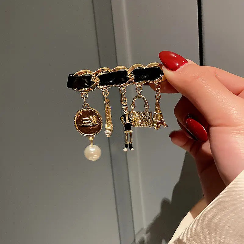 Black leather chain bracelet adorned with gold-toned charms including a pearl and miniature Eiffel Tower inspired by the pearl flower number 5 gold brooch pin.