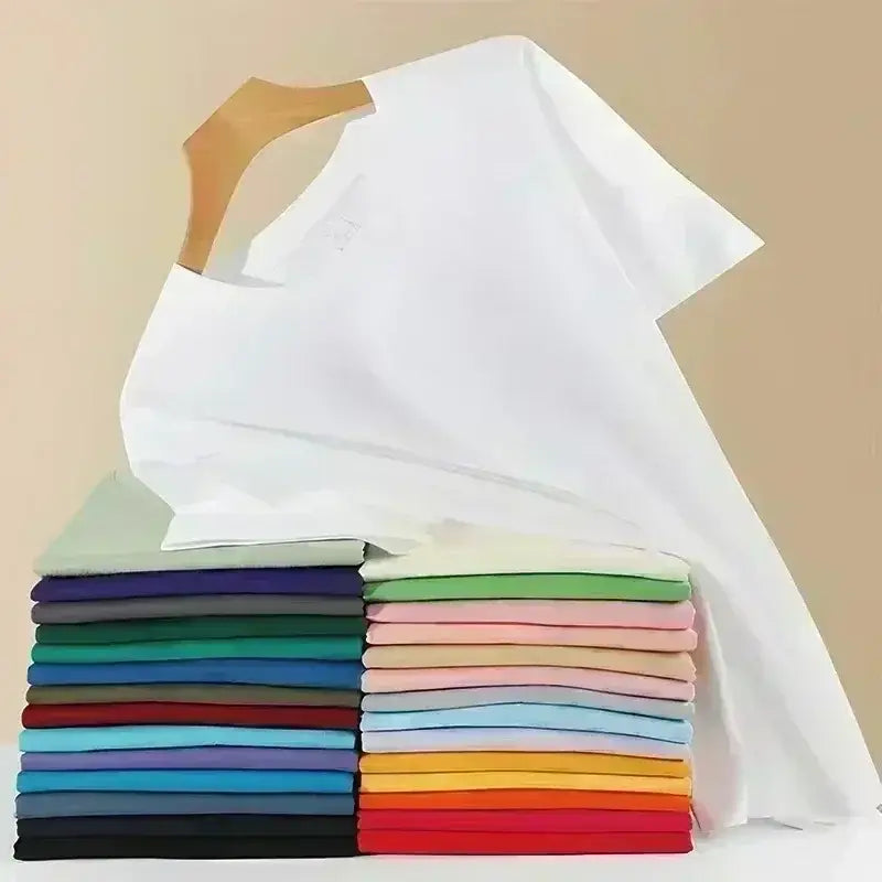 Una camiseta de algodón de cuello redondo blanco impecable, drapeada sobre una percha de madera y apoyada sobre una pila vibrante de camisetas de colores sólidos dobladas con esmero, incluida una camiseta de algodón de cuello redondo color azul marino.