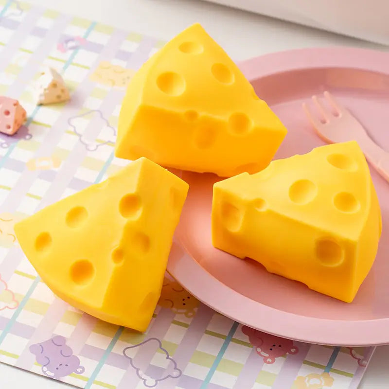 Trois éponges de bain en silicone jaune vif en forme de fromage, qui s’écrase, avec des trous caractéristiques, disposées sur une assiette rose, adaptées comme cadeaux pour les fêtes.