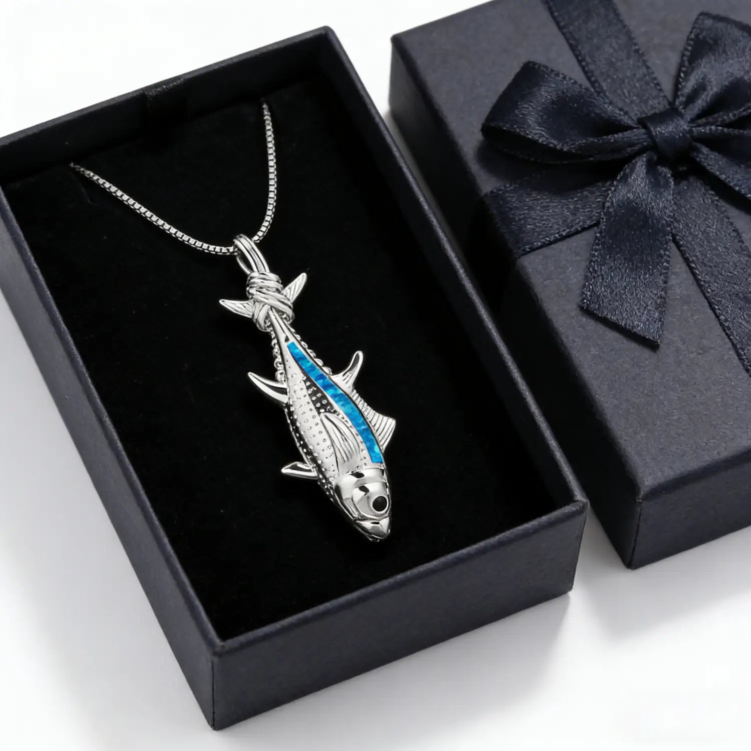 Collier pendentif en forme de poisson en argent, avec un placage d’opale bleue et une gravure détaillée, présenté dans une boîte doublée de velours noir, pour la collection de bijoux marins.