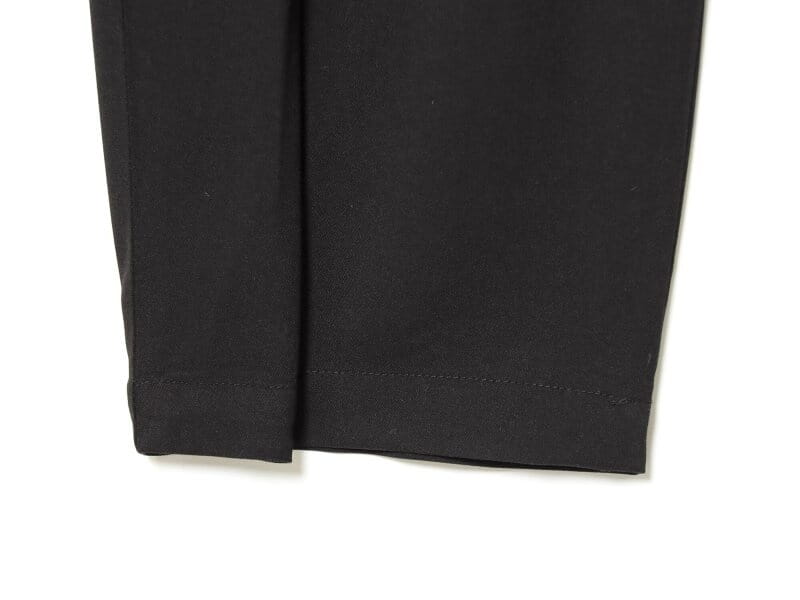 Pantalons noirs taille haute plissés à jambes évasées, présentant une coupe ajustée au niveau des jambes avec finition en tissu mat lisse et des coutures nettes le long de l’ourlet.
