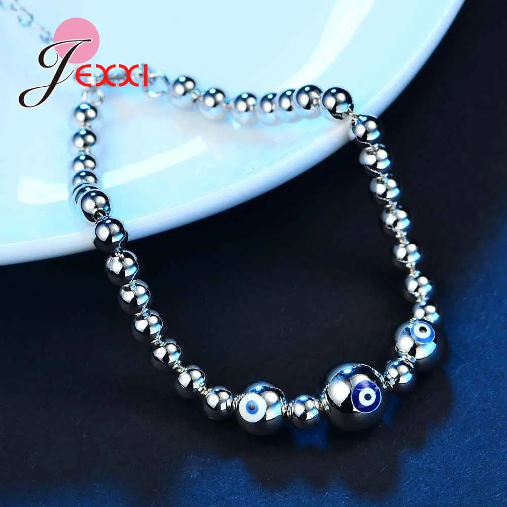 Sterling silver evil eye charm bracelet for women featuring alternating polished metallic spheres and distinctive blue evil eye beads.