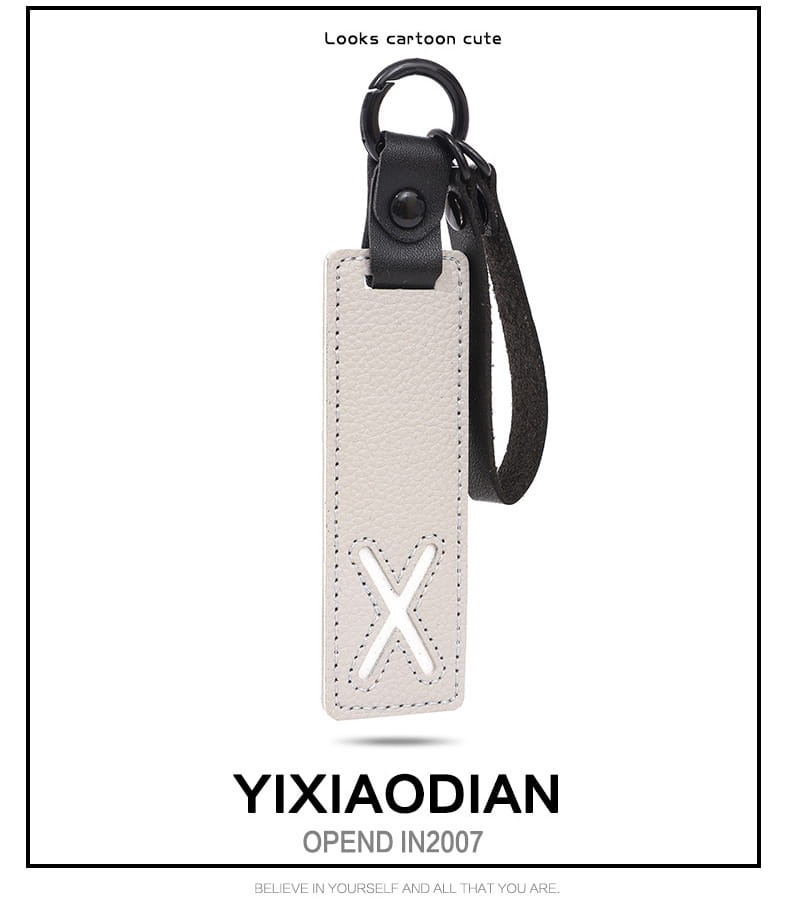 A sleek white leather letter keychain with an embossed x design, featuring a black strap and metal ring, ideal as an alphabet pendant party gift.