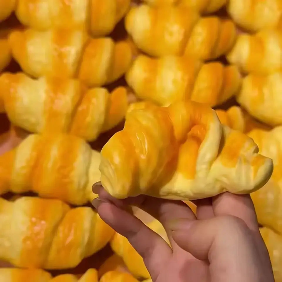 jouet anti-stress en forme de croissant feuilleté doré, tenu à la main, conçu pour soulager le stress et fabriqué en matériau souple