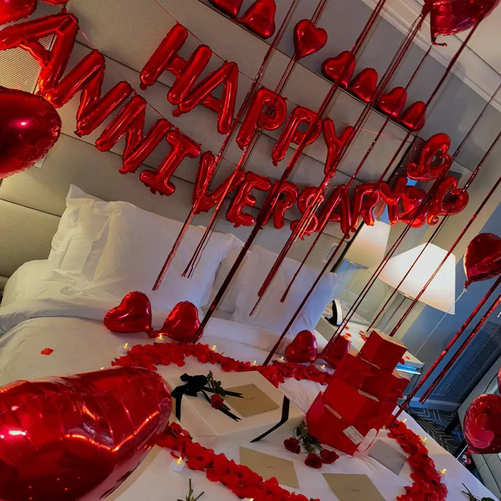 anniversary decoration set featuring red metallic balloon letters spelling happy anniversary with dangling heart shaped balloons and rose petals.