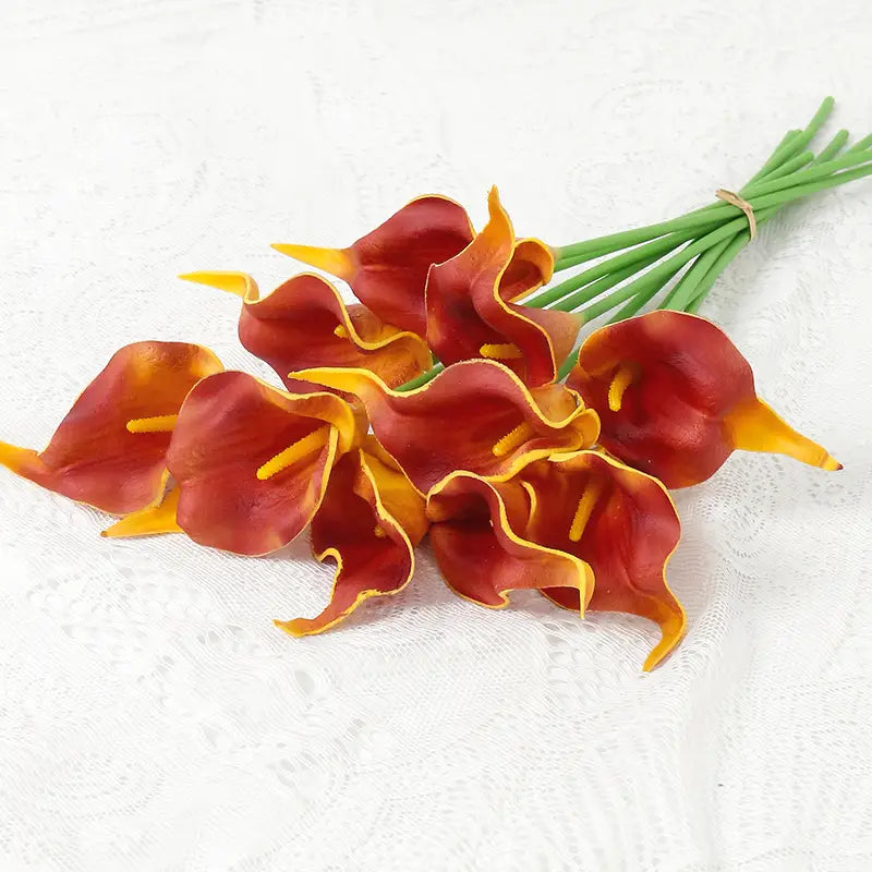 a bouquet of artificial red and yellow calla lilies with green stems tied together for home decor